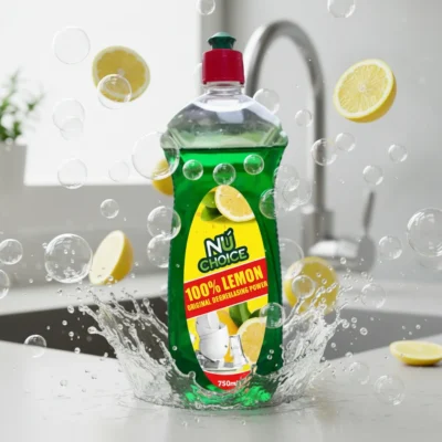 NuChoice 100% Lemon Dishwashing Liquid 750ml bottle with green liquid and red cap, surrounded by lemon slices, bubbles, and water splash on a kitchen countertop near a sink.